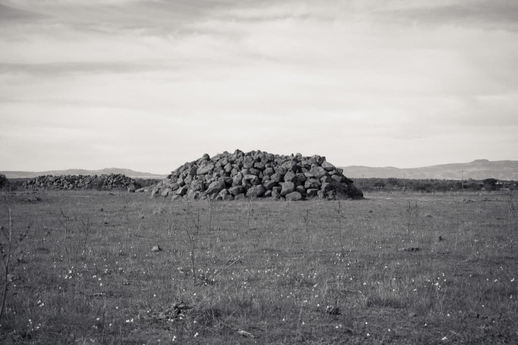 A cairn of dark stones in an open field.