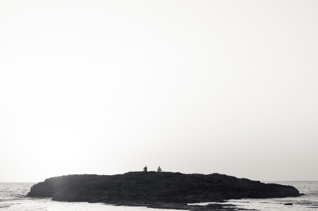 Two figures standing on a small island in a pale sea.