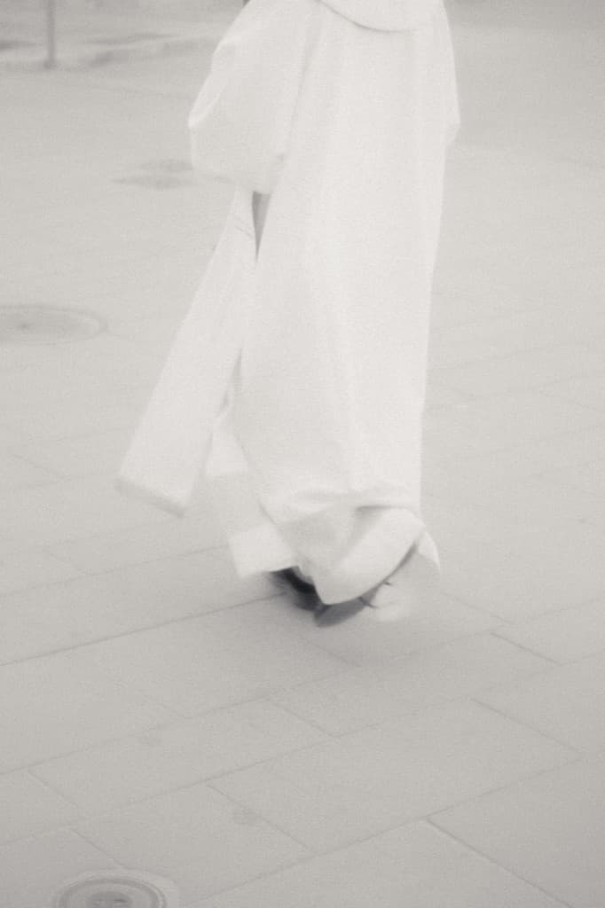 Someone in white walking across stone pavement.