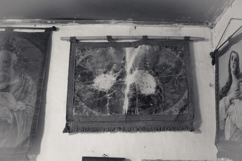 Torn religious tapestries on a white wall.