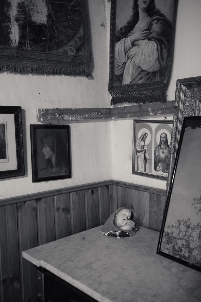 A shrine corner with prints, a marble slab, and a broken madonna.
