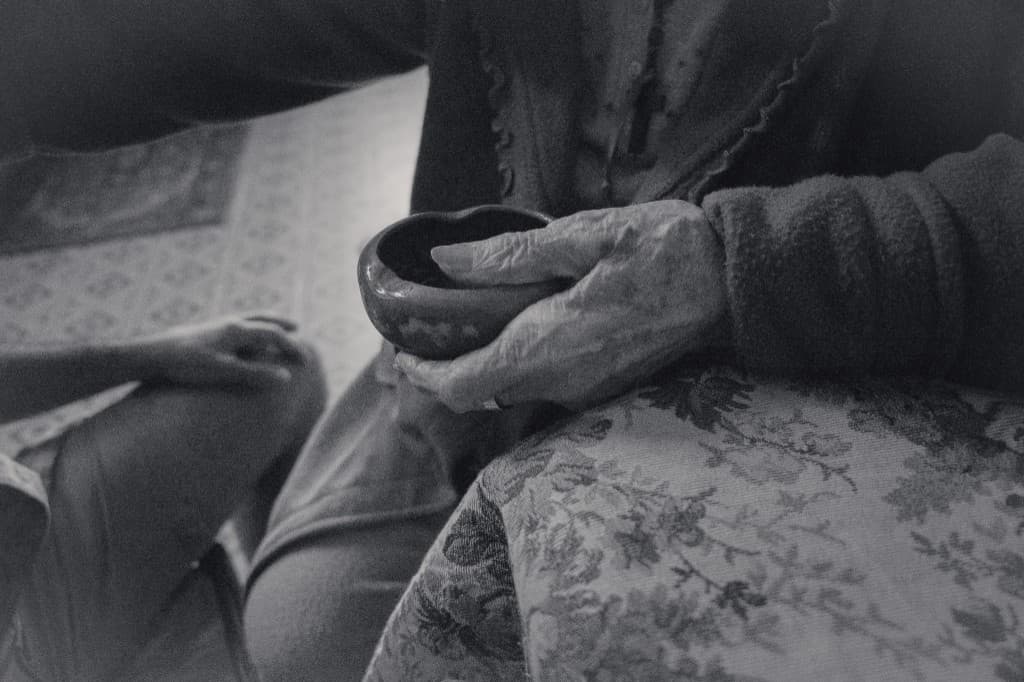 An old hand holding a small bowl.